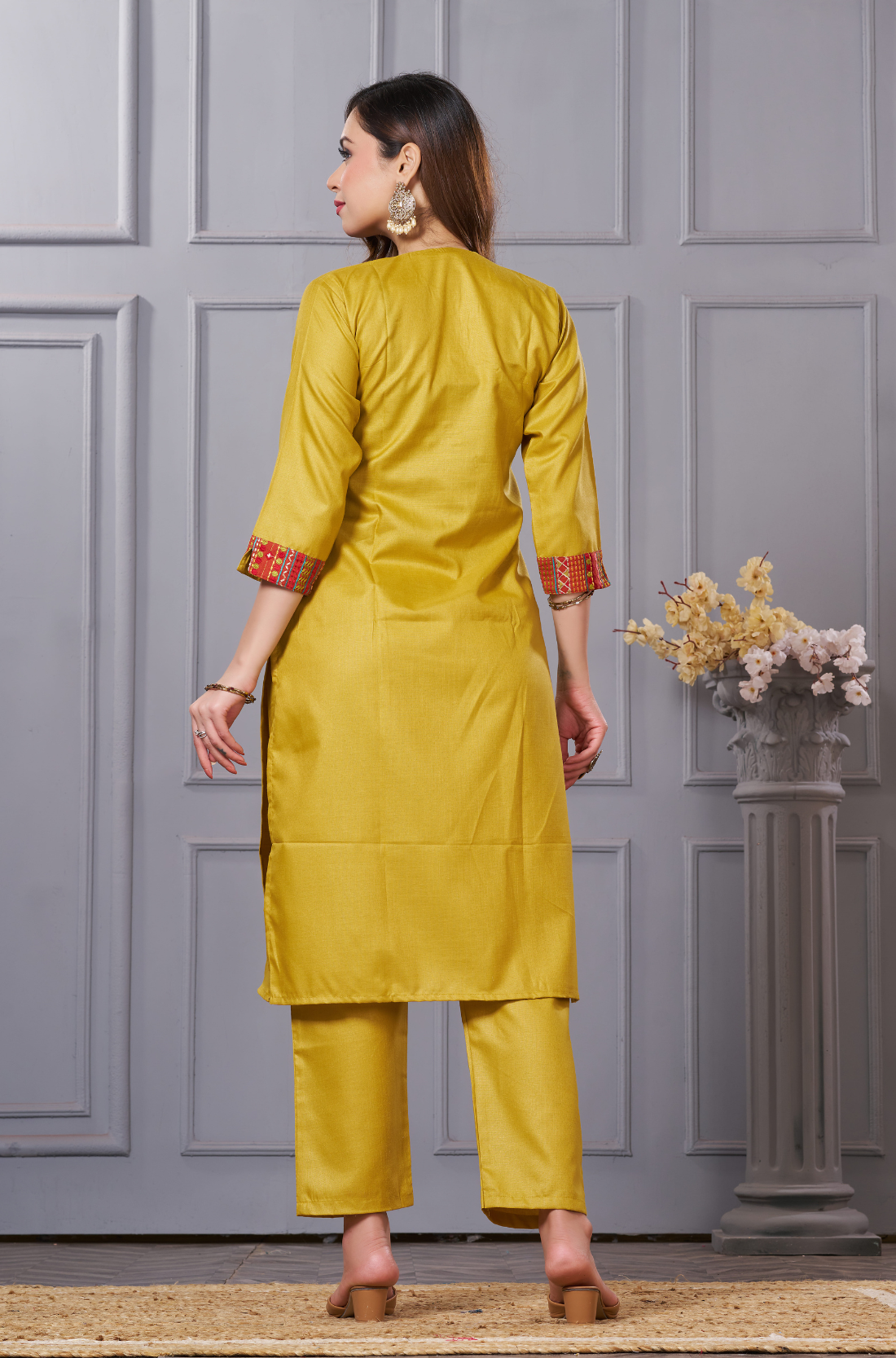 The back view of a mustard-yellow kurta set - highlighting the matching embroidered borders on the sleeves - and the structured fit of the trousers.