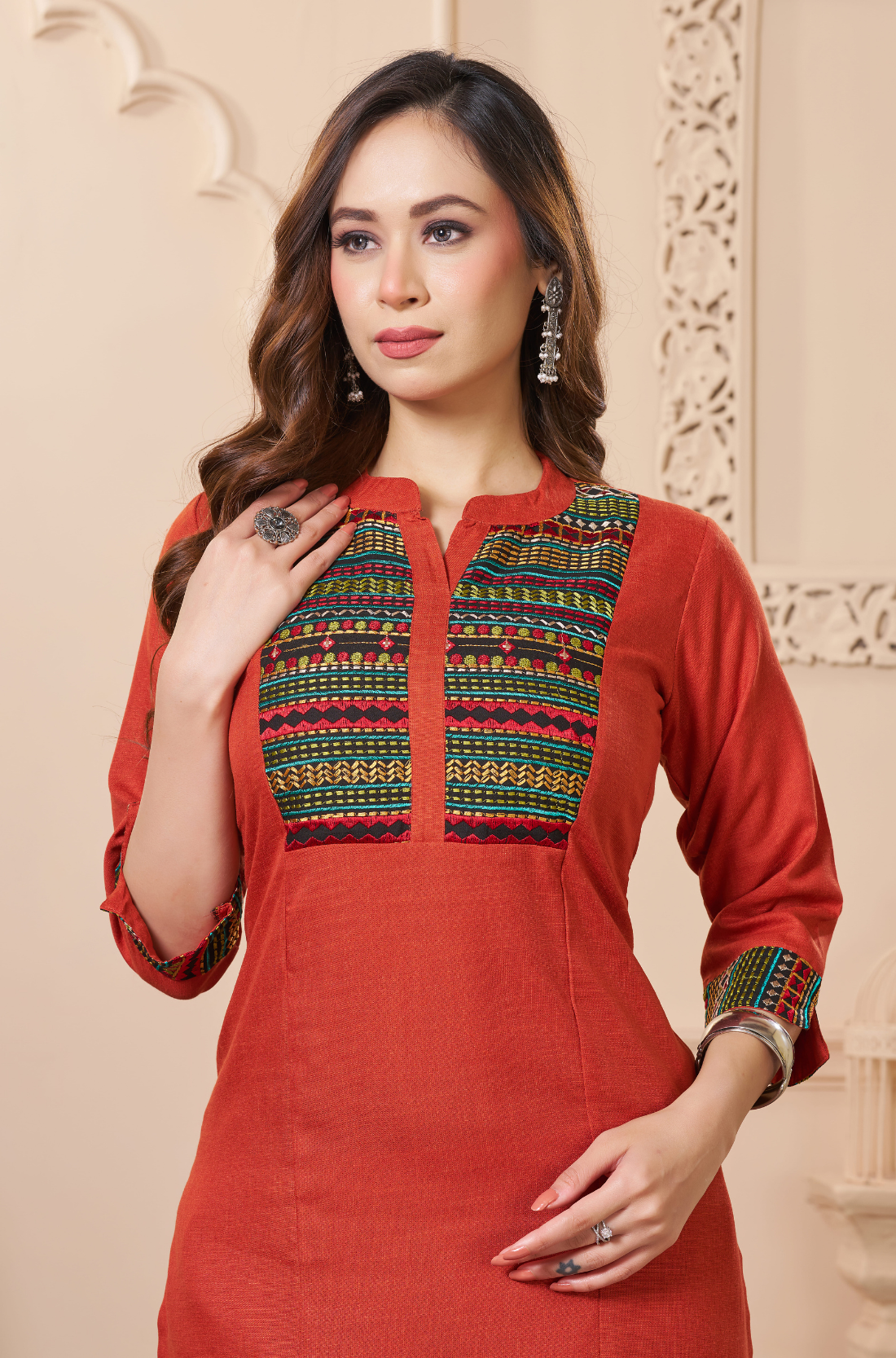 A close-up shot of the rust-orange kurta - focusing on the intricate horizontal embroidery in green, gold, and red - across the chest panel.