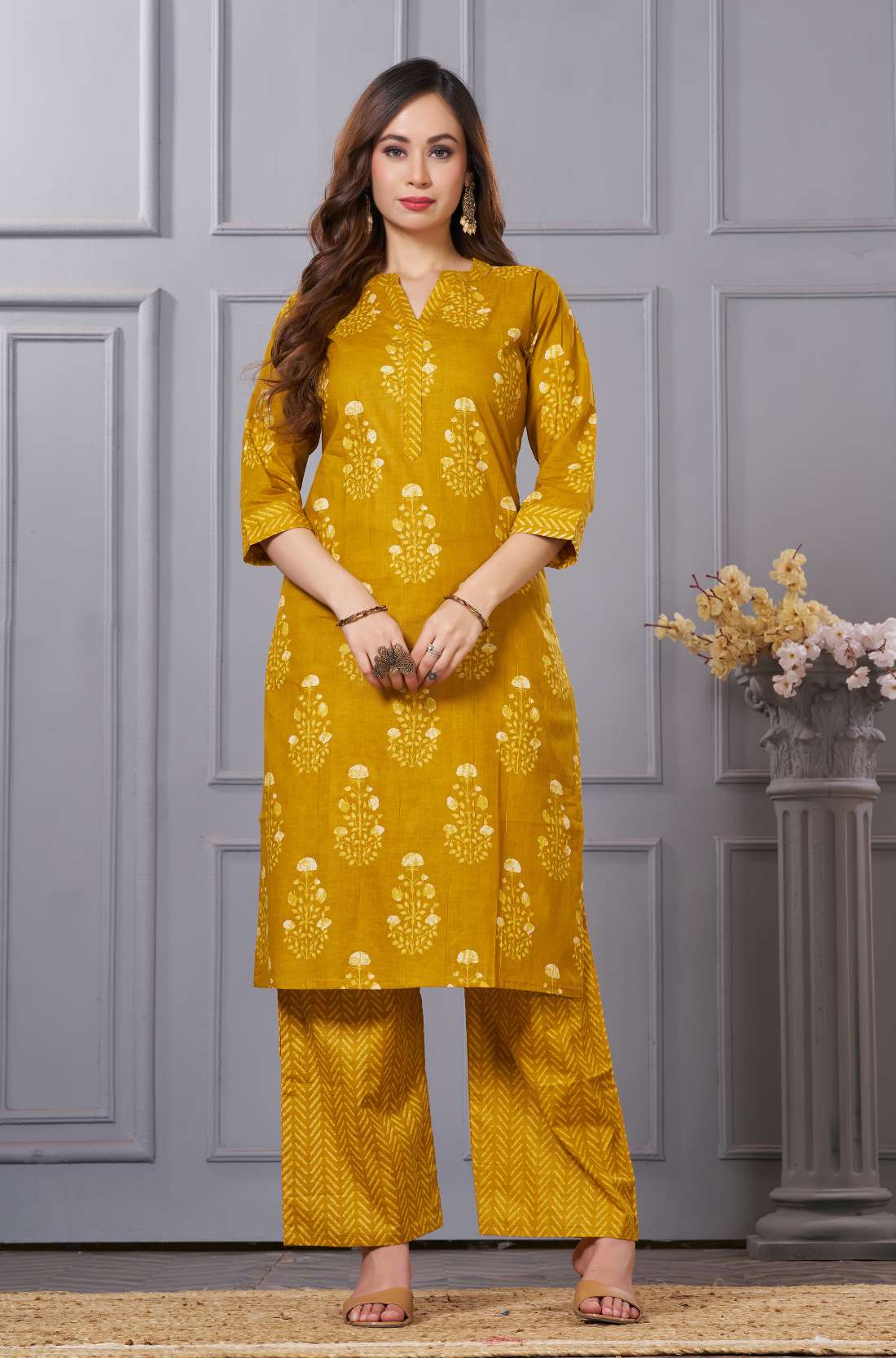 A woman posing in a rich teal blue straight kurta - featuring an intricate multicolored paisley embroidered yoke - and matching teal trousers.