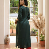 Back view of women's bottle green rayon kurti with a straight silhouette, round neckline, side slits and 3/4 sleeves, styled with red pants.