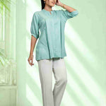 Women's sea green rayon shirt with a mandarin collar, front button placket, soft pleats, and half sleeves styled with white trousers for office and everyday wear.