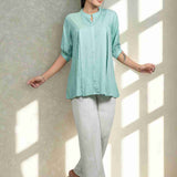 Front view of women's sea green rayon shirt featuring a mandarin collar, button-down front, front pleats, half sleeves, and a relaxed fit paired with white trousers.