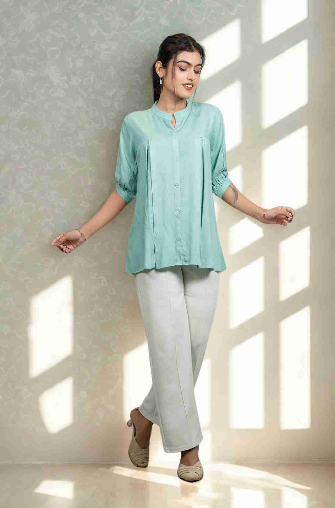 Front view of women's sea green rayon shirt featuring a mandarin collar, button-down front, front pleats, half sleeves, and a relaxed fit paired with white trousers.