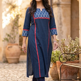 Woman walking outdoors on a cobbled path wearing a stylish blue kurta with red panel borders and dark blue trousers.