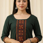 Close up shot of a bottle green rayon ethnic kurti for women featuring elegant red and gold geometric embroidery panel on the front bodice and matching trim borders on the three quarter sleeves.