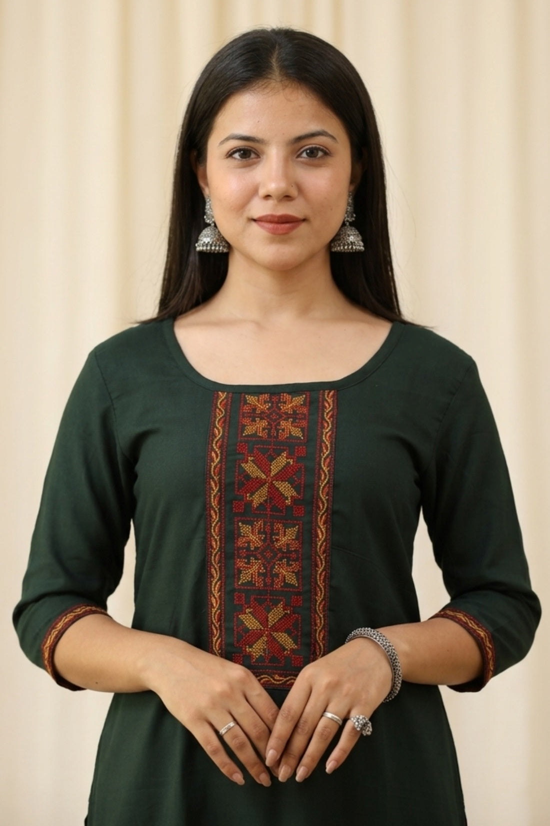 Close up shot of a bottle green rayon ethnic kurti for women featuring elegant red and gold geometric embroidery panel on the front bodice and matching trim borders on the three quarter sleeves.