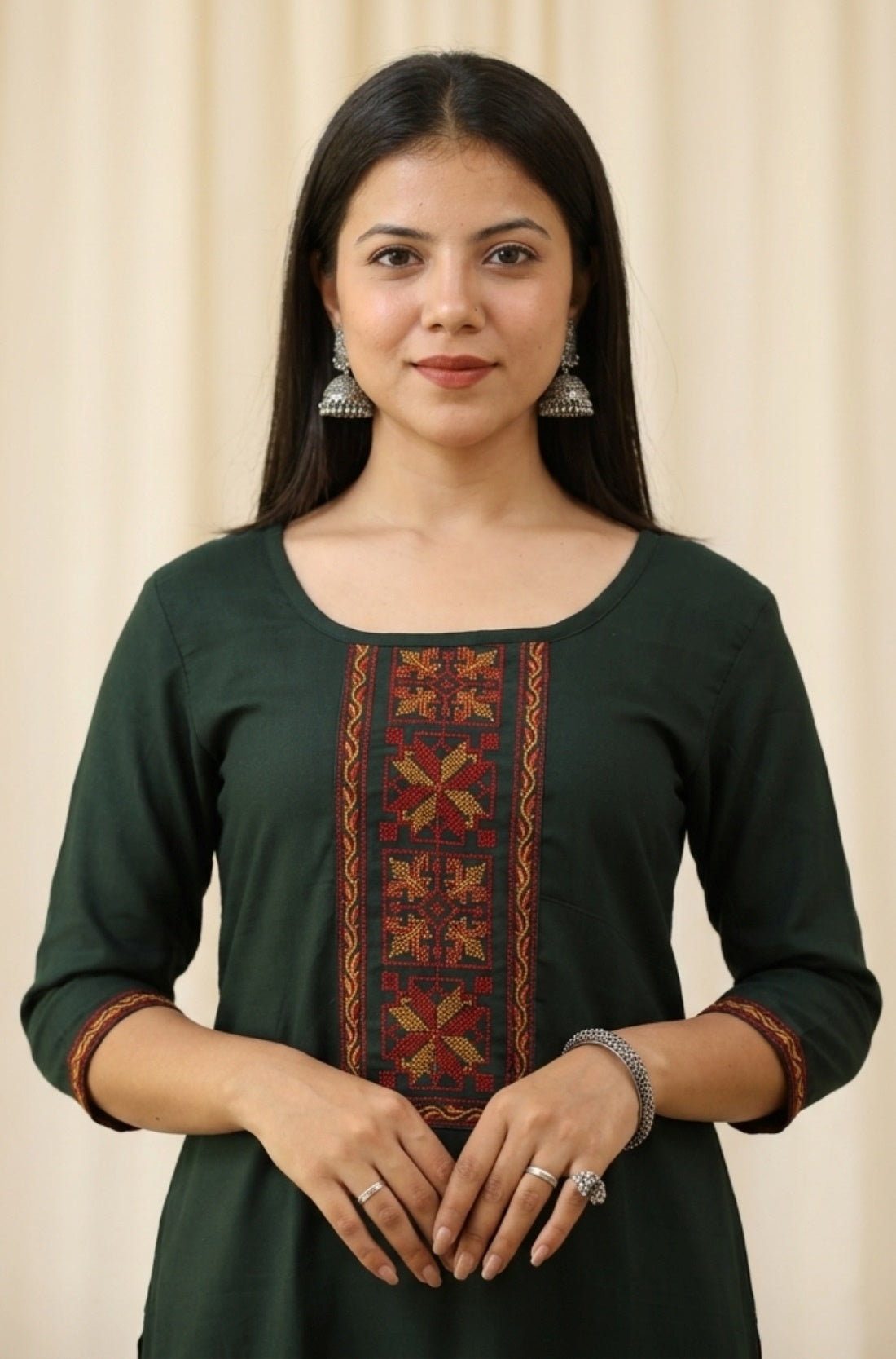 Close up shot of a bottle green rayon ethnic kurti for women featuring elegant red and gold geometric embroidery panel on the front bodice and matching trim borders on the three quarter sleeves.