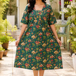 Full-length front view of a woman wearing a dark green pure cotton frock-style kurti featuring an all-over vibrant red and cream floral print, styled in a relaxed, flared silhouette.