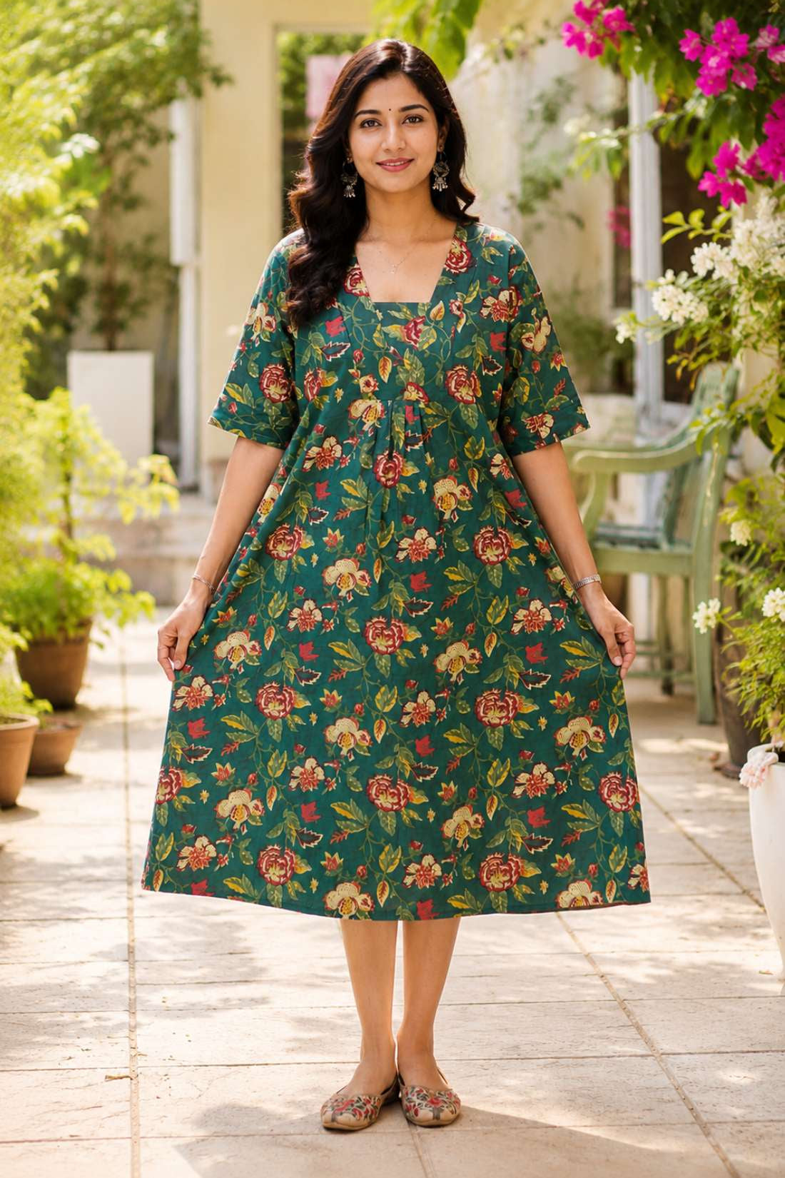 Full-length front view of a woman wearing a dark green pure cotton frock-style kurti featuring an all-over vibrant red and cream floral print, styled in a relaxed, flared silhouette.