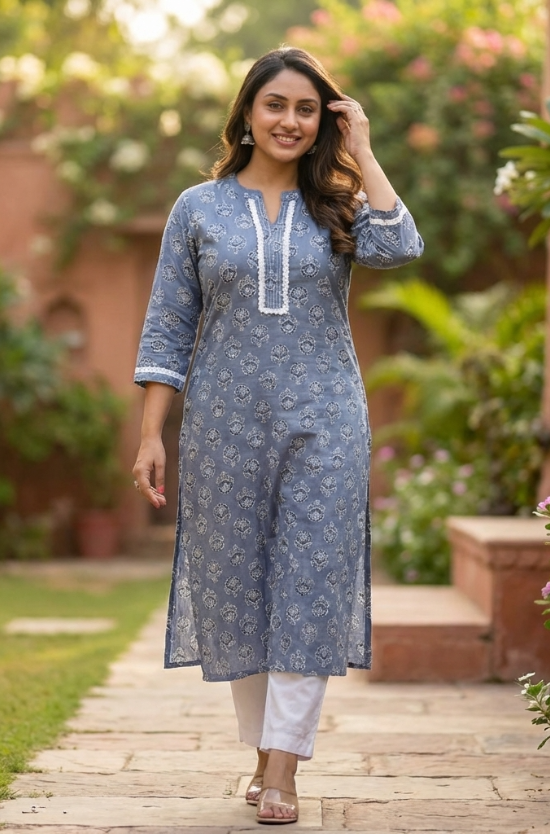 A woman walking gracefully in a garden wearing a grey-blue floral printed kurta and white straight pants.
