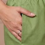 Close up view showcasing a functional side utility pocket tailored into a light green pure cotton kurta with vibrant floral cross stitch embroidery details, with a hand resting inside the pocket over straight pants.