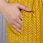 Close up view of the functional side utility pocket stitched seamlessly into a floral cotton straight kurta, showing a hand resting inside the pocket over contrasting purple chevron print trousers.