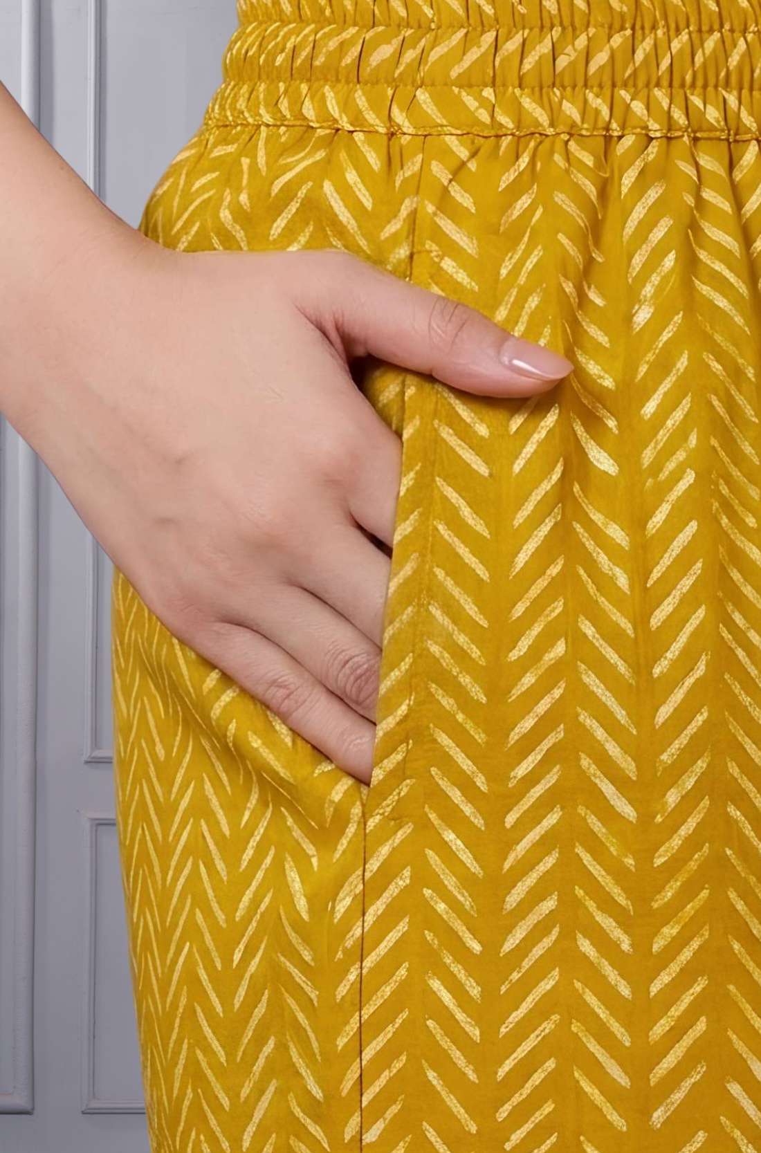 Close up view of the functional side utility pocket stitched seamlessly into a floral cotton straight kurta, showing a hand resting inside the pocket over contrasting purple chevron print trousers.