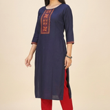 A woman standing in a navy blue straight kurta paired with red trousers, showcasing a professional ethnic look.
