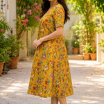 Side profile view of a woman wearing an ochre yellow cotton floral print frock-style kurti dress, showcasing the relaxed-fit elbow sleeves and A-line drape.