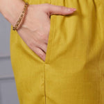 Close up view highlighting the functional side utility pocket tailored into the matching straight trousers of an ochre yellow cotton kurta set, showing a hand resting inside the pocket.