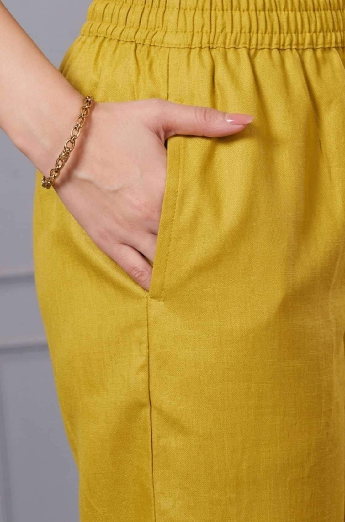 Close up view highlighting the functional side utility pocket tailored into the matching straight trousers of an ochre yellow cotton kurta set, showing a hand resting inside the pocket.