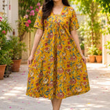 Full-length view of a woman showcasing a bright ochre yellow pure cotton frock-style kurti with an all-over traditional floral print in red and green hues.