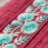A detailed macro close-up of a pink cotton kurta showing intricate turquoise and white floral thread embroidery work.