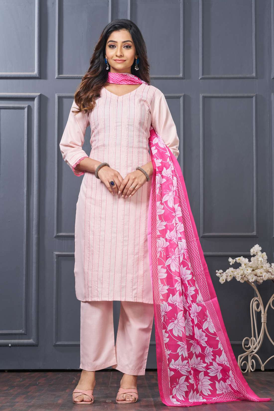 Front full length view of a model wearing a pink pure cotton kurta set featuring vertical pintucks and vibrant multicolor thread embroidery on the neckline, paired with straight trousers and a matching printed dupatta