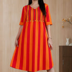 Model posing in a pure handloom cotton pintucks tunic in vibrant orange and red vertical stripes with embroidered V-neck detailing and elbow-length sleeves.