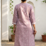 A rear view of a woman wearing a purple printed kurta with white trousers, highlighting the back silhouette.