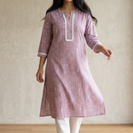 A woman standing in a purple printed ethnic kurta paired with white trousers, displaying a casual yet stylish look.