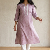 A woman standing in a purple printed ethnic kurta paired with white trousers, displaying a casual yet stylish look.