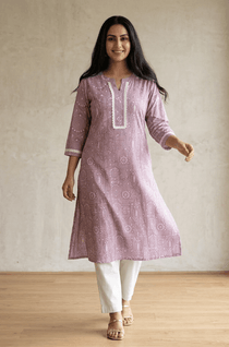 A woman standing in a purple printed ethnic kurta paired with white trousers, displaying a casual yet stylish look.