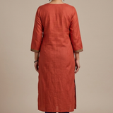 A full-length rear view of a woman modeling a rust-orange straight-cut kurta and blue pants.