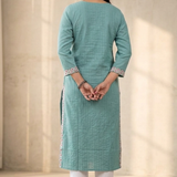 A rear view of a woman wearing a sea-green straight-cut kurta paired with white trousers.