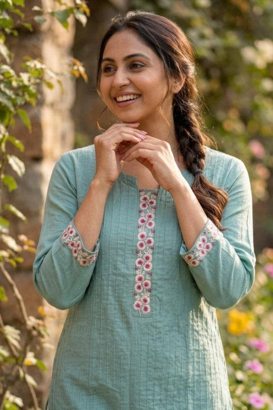 portrait.jpg	A woman posing with her hands near her face, wearing a sea-green embroidered kurta in a garden 