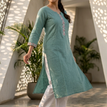 A woman walking in a garden wearing a sea-green kurta, showcasing the flow and drape of the fabric.
