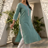 A woman walking in a garden wearing a sea-green kurta, showcasing the flow and drape of the fabric.