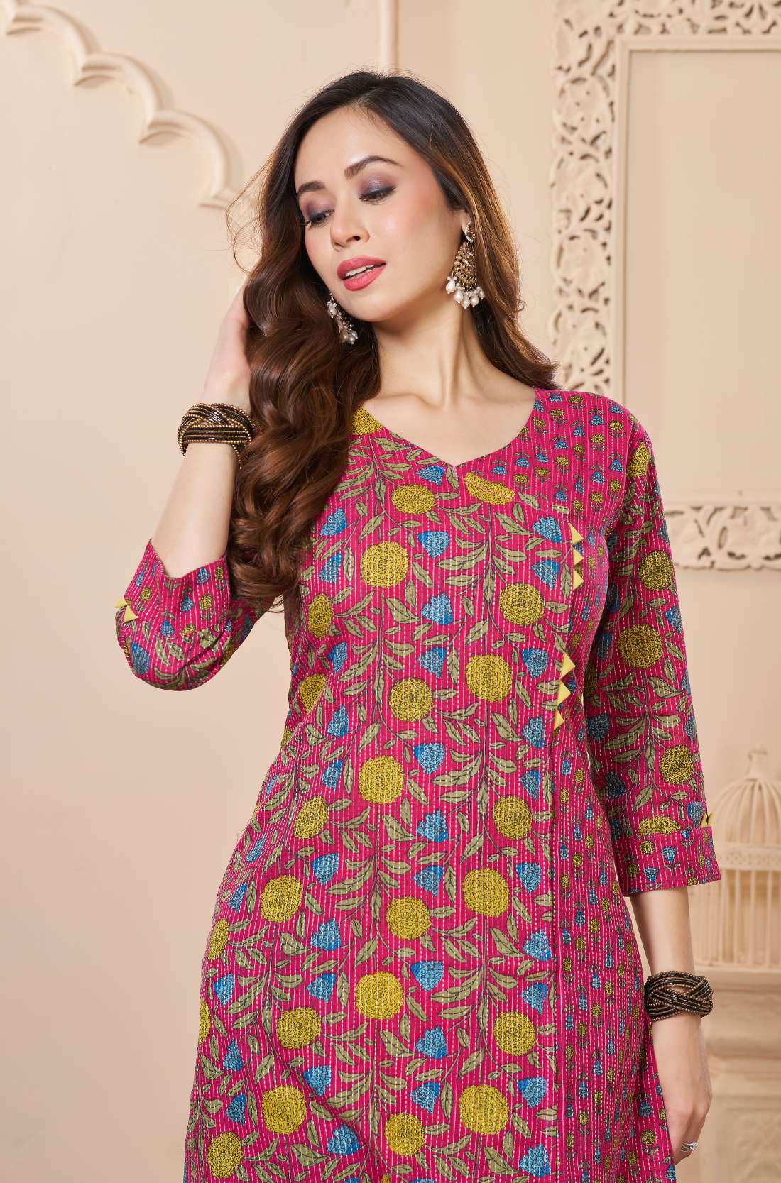 A woman posing in a deep burgundy kurta - featuring a vertical floral vine print in blue and orange - paired with navy blue trousers.