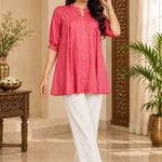 Full-length angled view of a model posing in a dark peach pleated rayon tunic with elbow-length sleeves.
