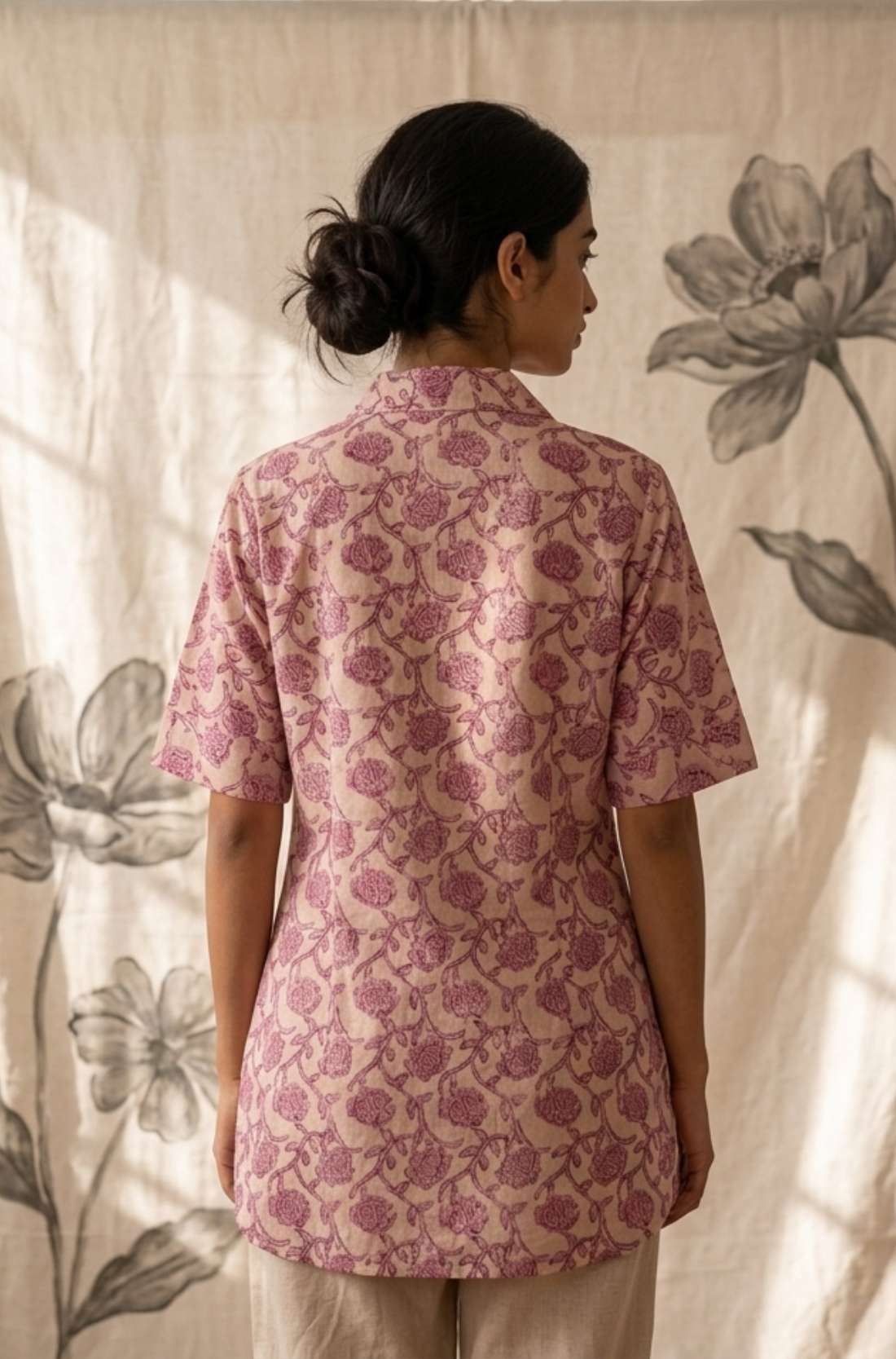 Back profile of a women's blush pink hand block print cotton shirt with short sleeves and curved hem.