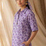 Side profile of a women's lavender floral block print cotton shirt paired with white trousers.