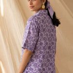 Back view of a women's lavender floral block print cotton shirt with short sleeves and curved hem.