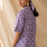Back view of a women's lavender floral block print cotton shirt with short sleeves and curved hem.