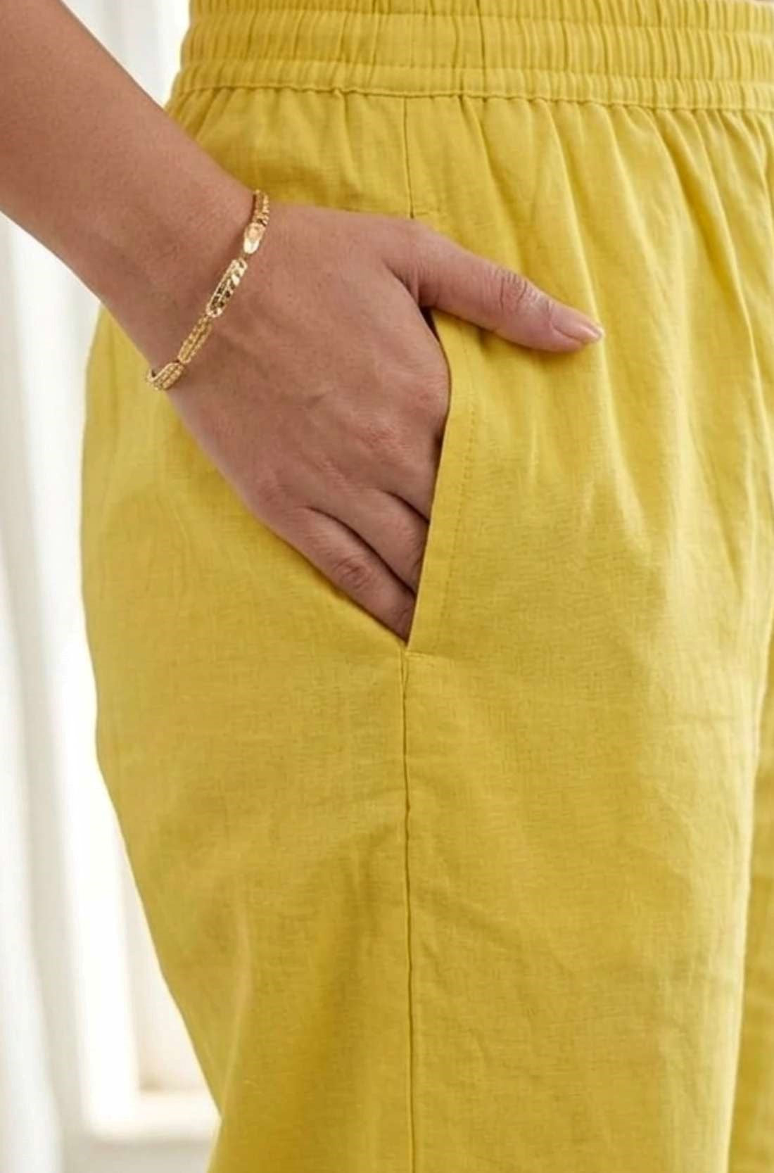 Close-up view highlighting the functional side utility pocket tailored into the matching yellow pure cotton straight-fit trousers, showing a model's hand resting inside the pocket.
