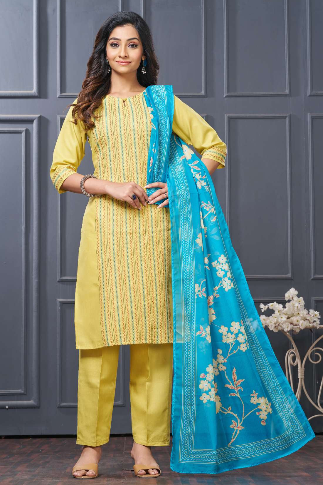 Front full length view of a model wearing a yellow pure cotton kurta set featuring vertical pintucks and vibrant multicolor thread embroidery on the neckline, paired with straight trousers and a matching printed dupatta